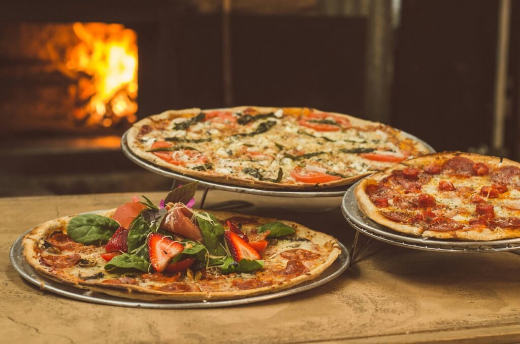 pexels-photo-1566837-1566837 Trio of gourmet pizzas with unique toppings near a wood-fired oven, ideal for food enthusiasts.