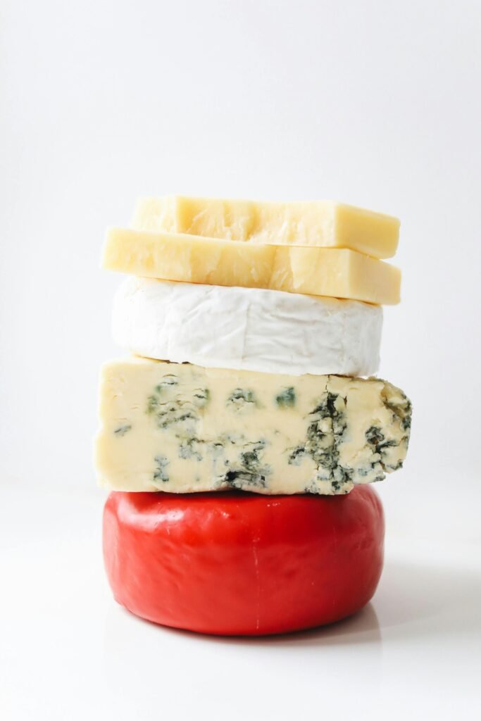 pexels-photo-4187779-4187779 Artistic stack of diverse gourmet cheeses on a white background.
